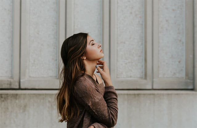 photo of woman with closed eyes while standing beside a wall