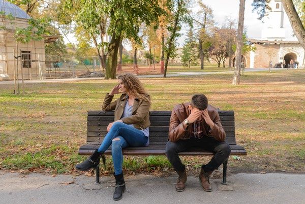 an and woman wearing jackets sitting in the bench not looking each other